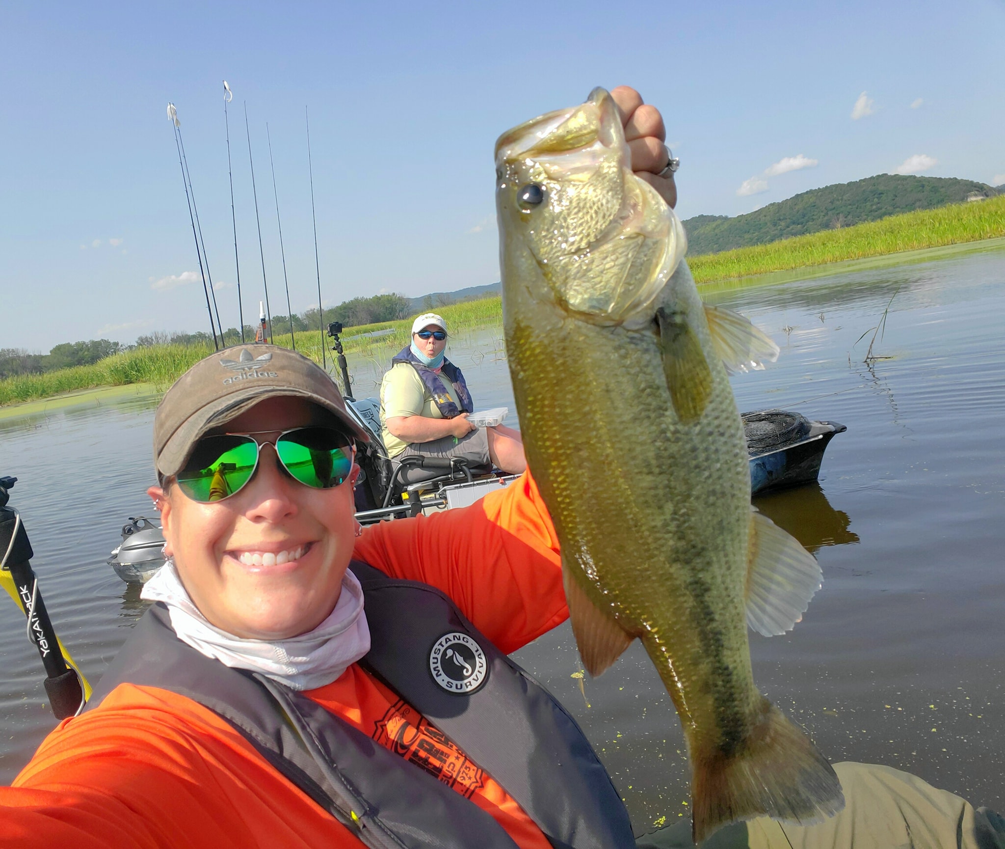 Susie photobombing Katie holding up a big largemouth bass